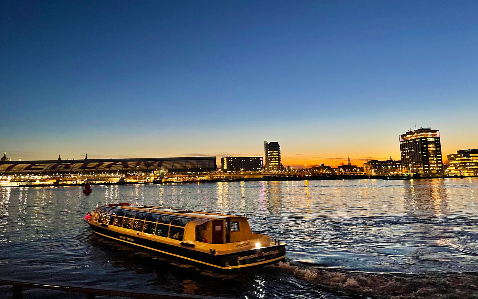 Amsterdam canal cruise boat at sunset with city skyline in the background.