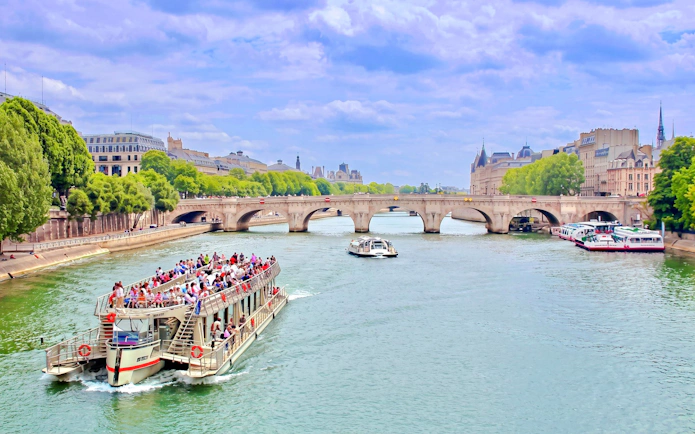 Seine River cruise boat with tourists near Paris bridge.