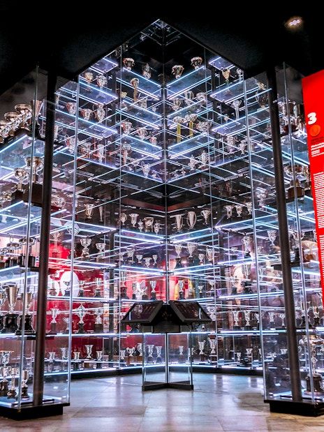 Benfica Stadium Museum trophy display with glass shelves and red backdrop.