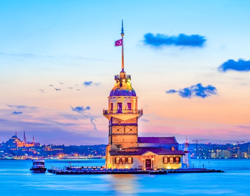 Maiden's Tower at sunset on the Bosphorus, Istanbul, with city skyline in the background.