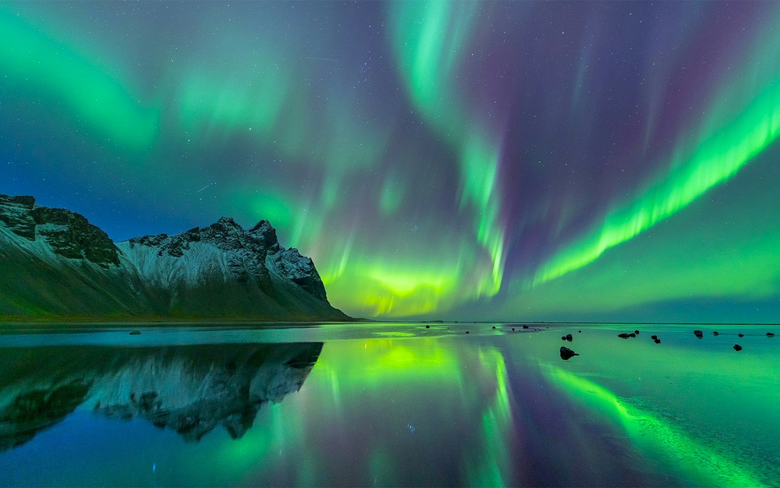 Northern lights over a lake in Tromso, Norway, with snowy mountains in the background.