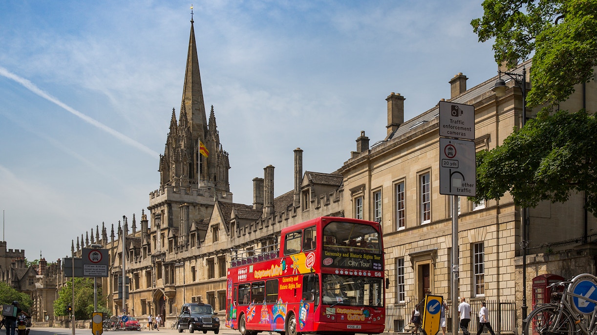 Open-top tour bus passing historic Oxford architecture.
