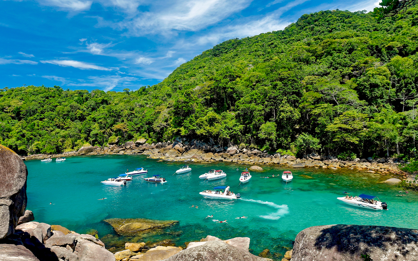 Boats and swimmers in a turquoise bay surrounded by lush forest on Ilha Grande, Rio de Janeiro.