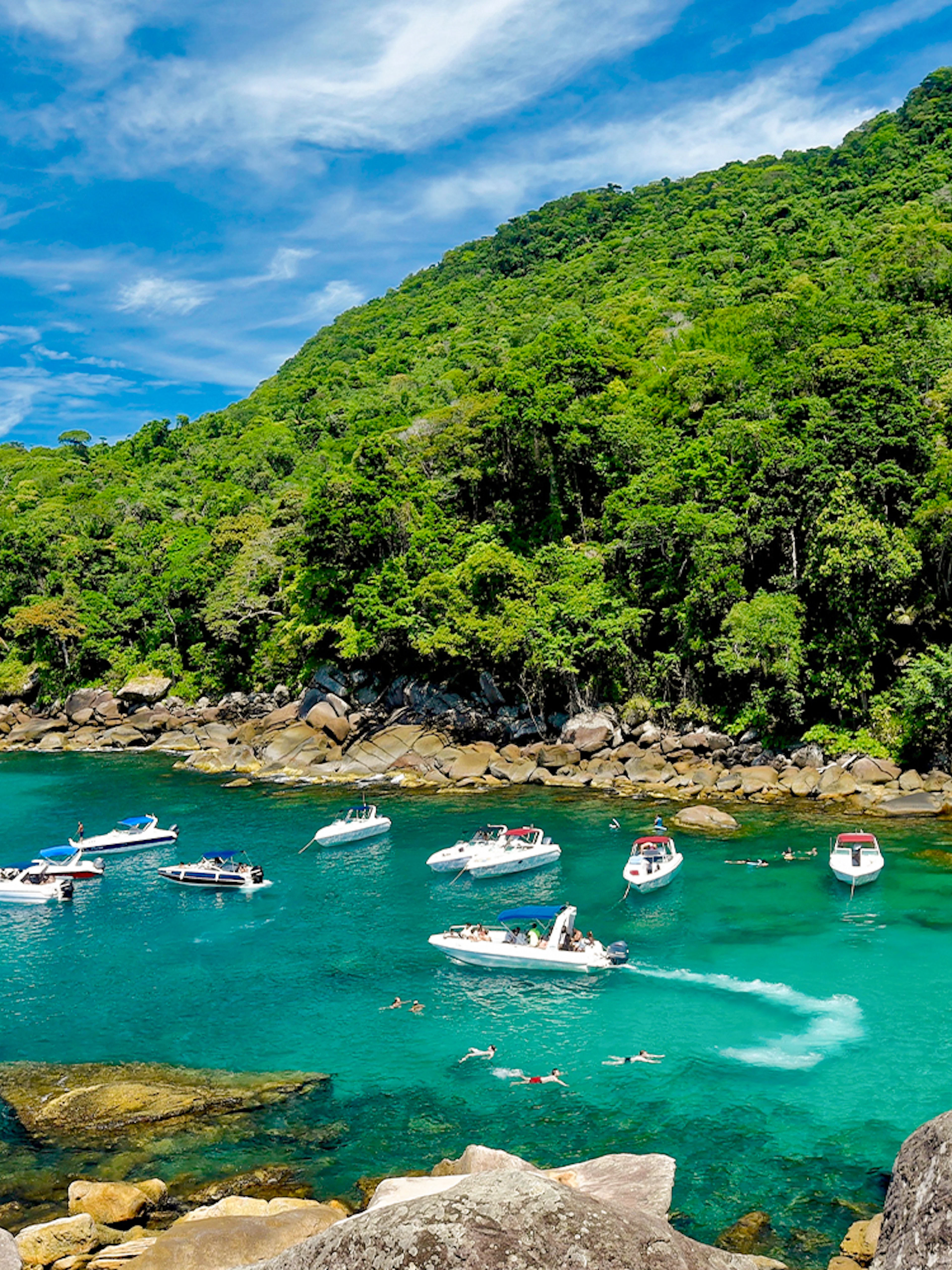 Boats and swimmers in a turquoise bay surrounded by lush forest on Ilha Grande, Rio de Janeiro.