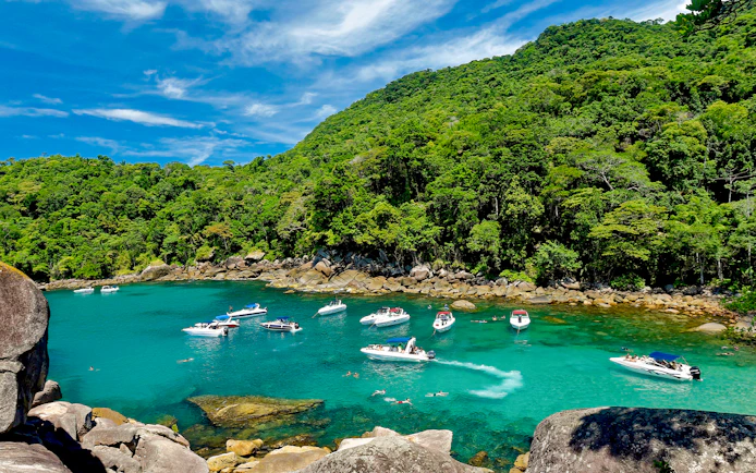 Boats and swimmers in a turquoise bay surrounded by lush forest on Ilha Grande, Rio de Janeiro.
