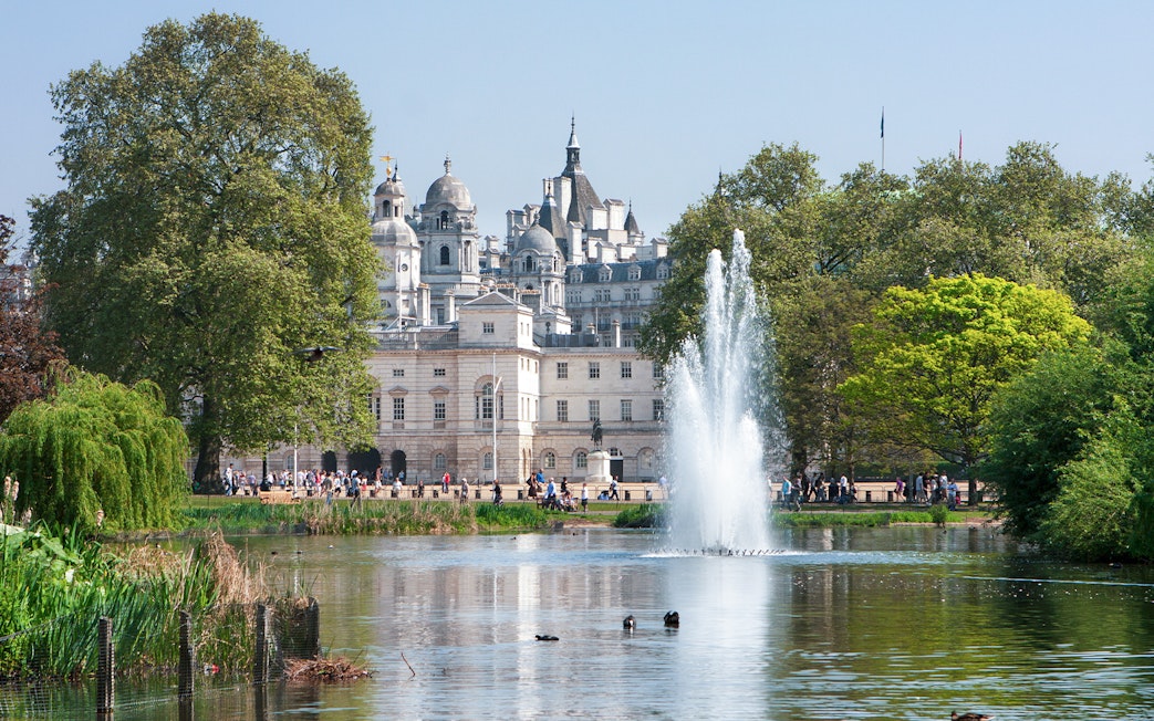 Fountain and trees in St James's Park with historic buildings in London.