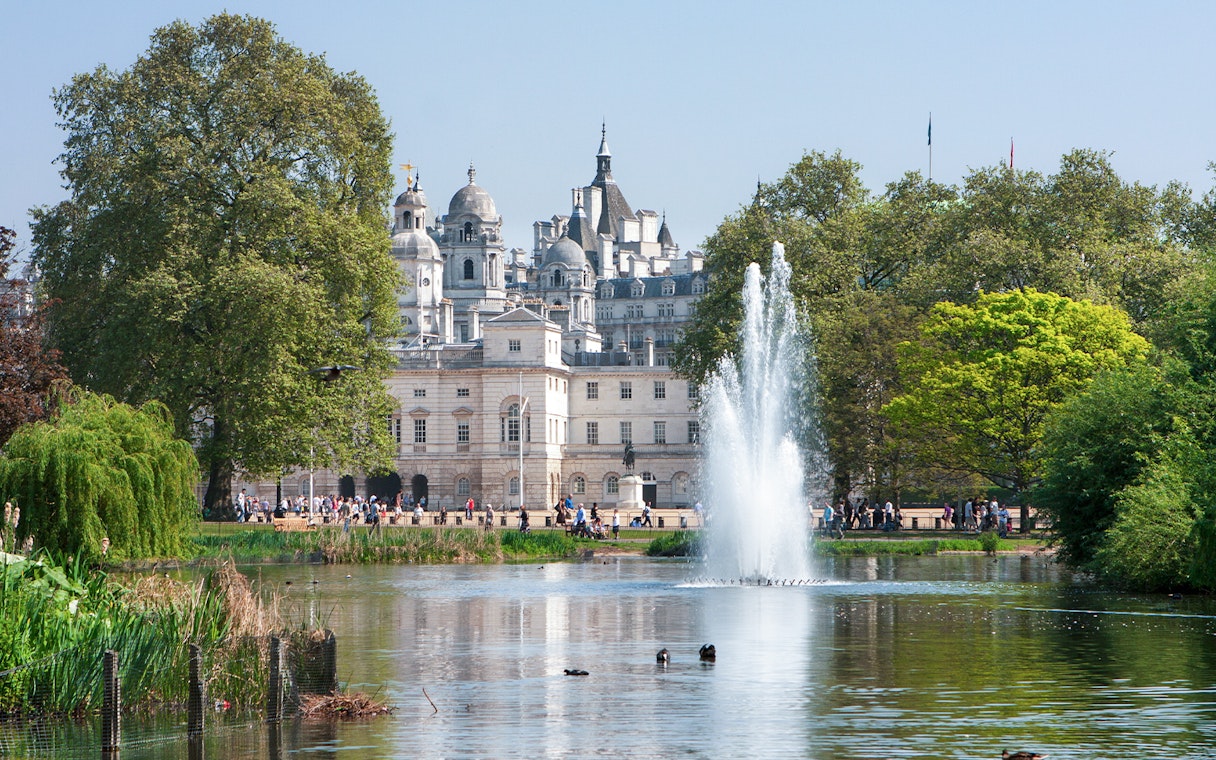 Fountain and trees in St James's Park with historic buildings in London.