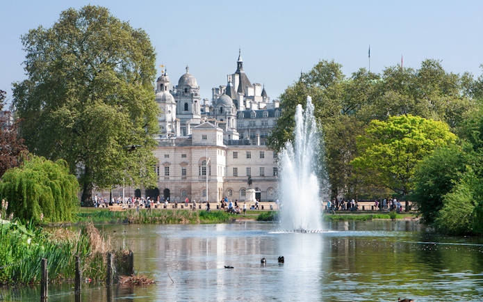 Fountain and trees in St James's Park with historic buildings in London.