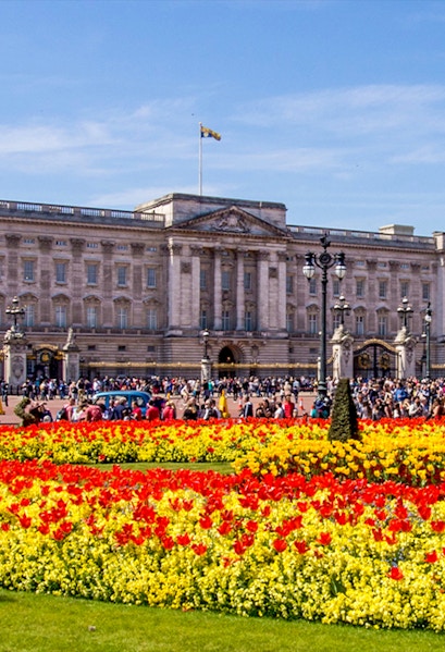 Buckingham Palace with colorful flower gardens and visitors in London.