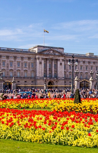 Buckingham Palace with colorful flower gardens and visitors in London.