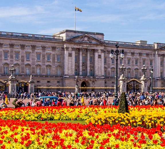 Buckingham Palace with colorful flower gardens and visitors in London.