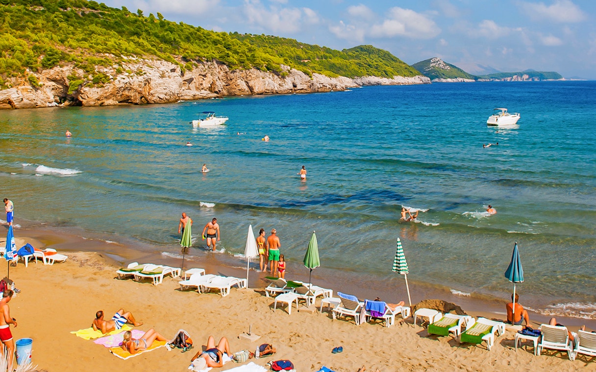 Tourists enjoying Sunj Beach on Lopud Island with boats in the Adriatic Sea.