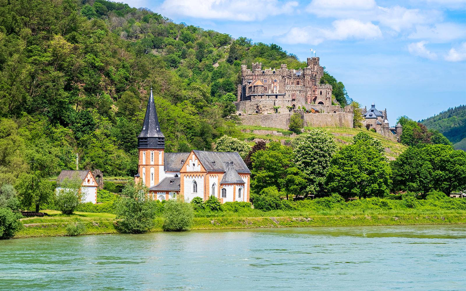 Church and castle in lush landscape along the Rhine River, Middle Rhine Valley, Germany.