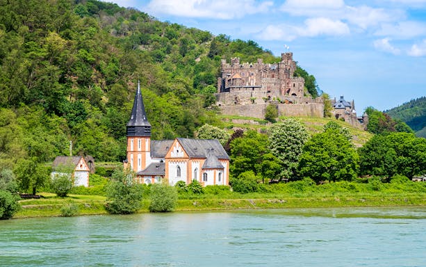 Church and castle in lush landscape along the Rhine River, Middle Rhine Valley, Germany.