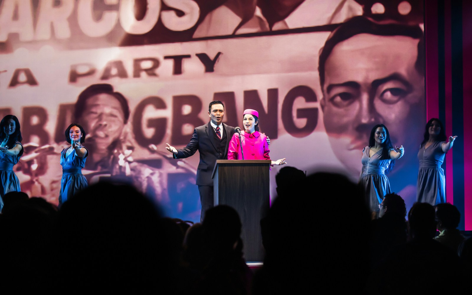 Performers on stage during "Here Lies Love" musical with historical backdrop.