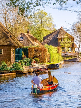 Boating through Giethoorn canal with thatched houses and lush greenery, Giethoorn, Netherlands.