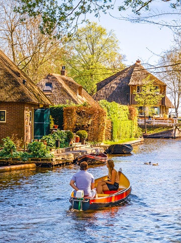 Boating through Giethoorn canal with thatched houses and lush greenery, Giethoorn, Netherlands.