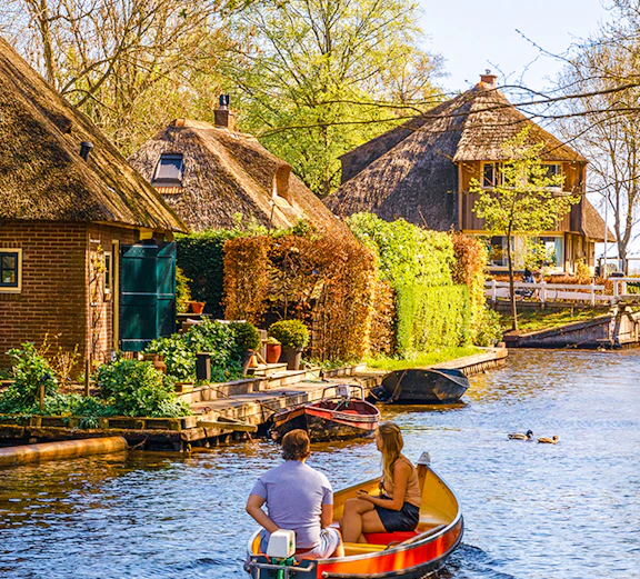 Boating through Giethoorn canal with thatched houses and lush greenery, Giethoorn, Netherlands.