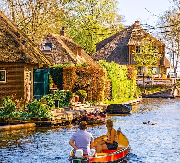 Boating through Giethoorn canal with thatched houses and lush greenery, Giethoorn, Netherlands.