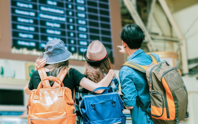 Friends with backpacks looking at train schedule in railway station.