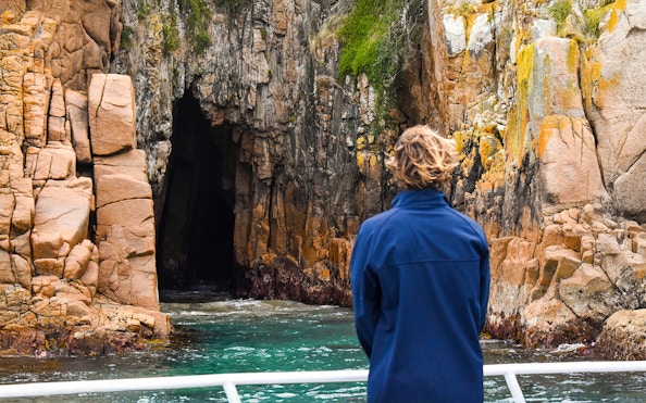 Person viewing rocky cliffs and cave from a boat on Cape Woolamai cruise, Phillip Island.