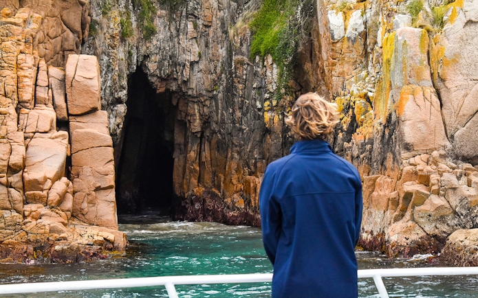 Person viewing rocky cliffs and cave from a boat on Cape Woolamai cruise, Phillip Island.