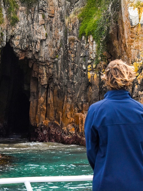 Person viewing rocky cliffs and cave from a boat on Cape Woolamai cruise, Phillip Island.