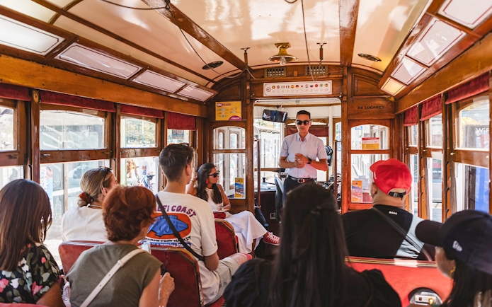 Tour guide speaking to passengers on a Lisbon tram during a hop-on hop-off tour.