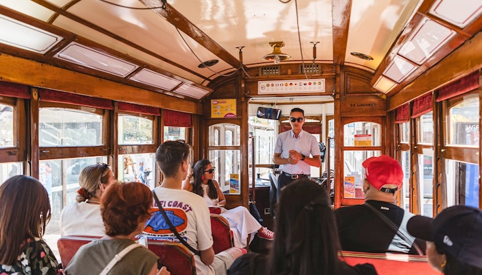 Tour guide speaking to passengers on a Lisbon tram during a hop-on hop-off tour.