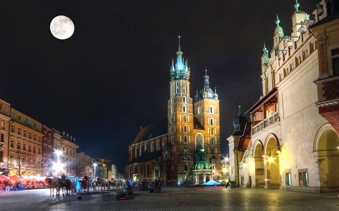 Krakow's Main Square at night with St. Mary's Basilica under a full moon.