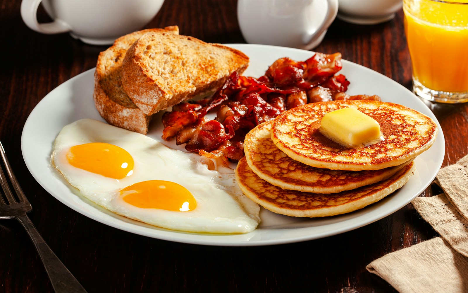 Traditional Canadian breakfast with eggs, pancakes, bacon, and toast on a plate.