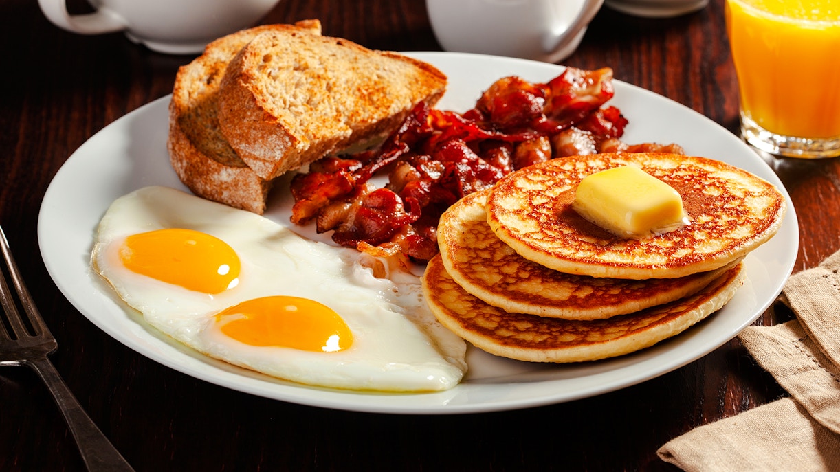 Traditional Canadian breakfast with eggs, pancakes, bacon, and toast on a plate.
