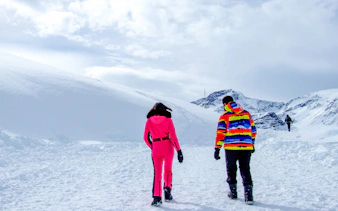Two people walking on a snowy path in Valle Nevado, Santiago, with mountains in the background.