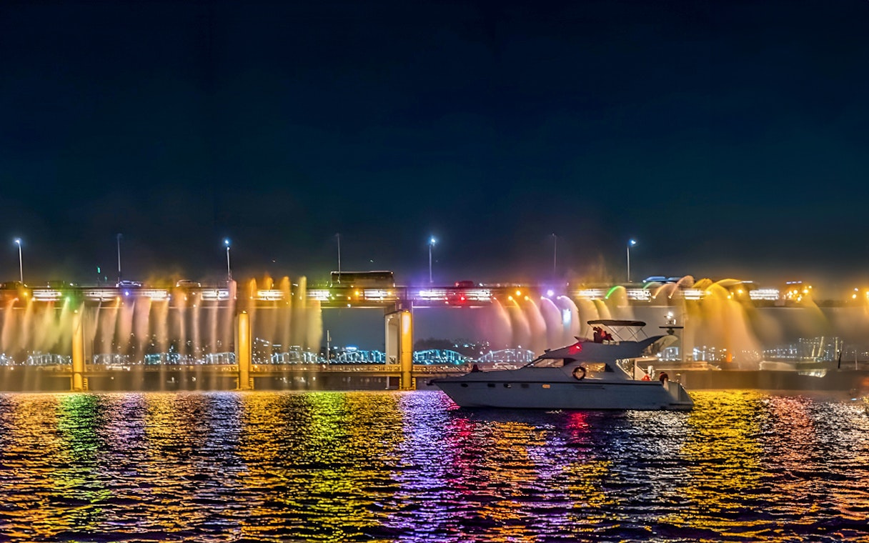 Yacht on Han River at night with colorful bridge lights in Seoul.