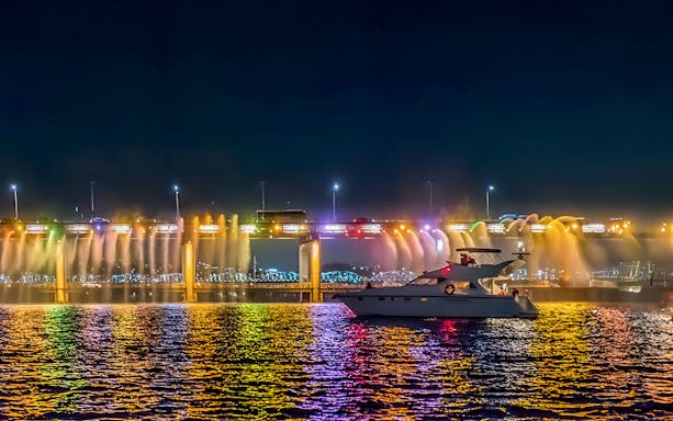 Yacht on Han River at night with colorful bridge lights in Seoul.