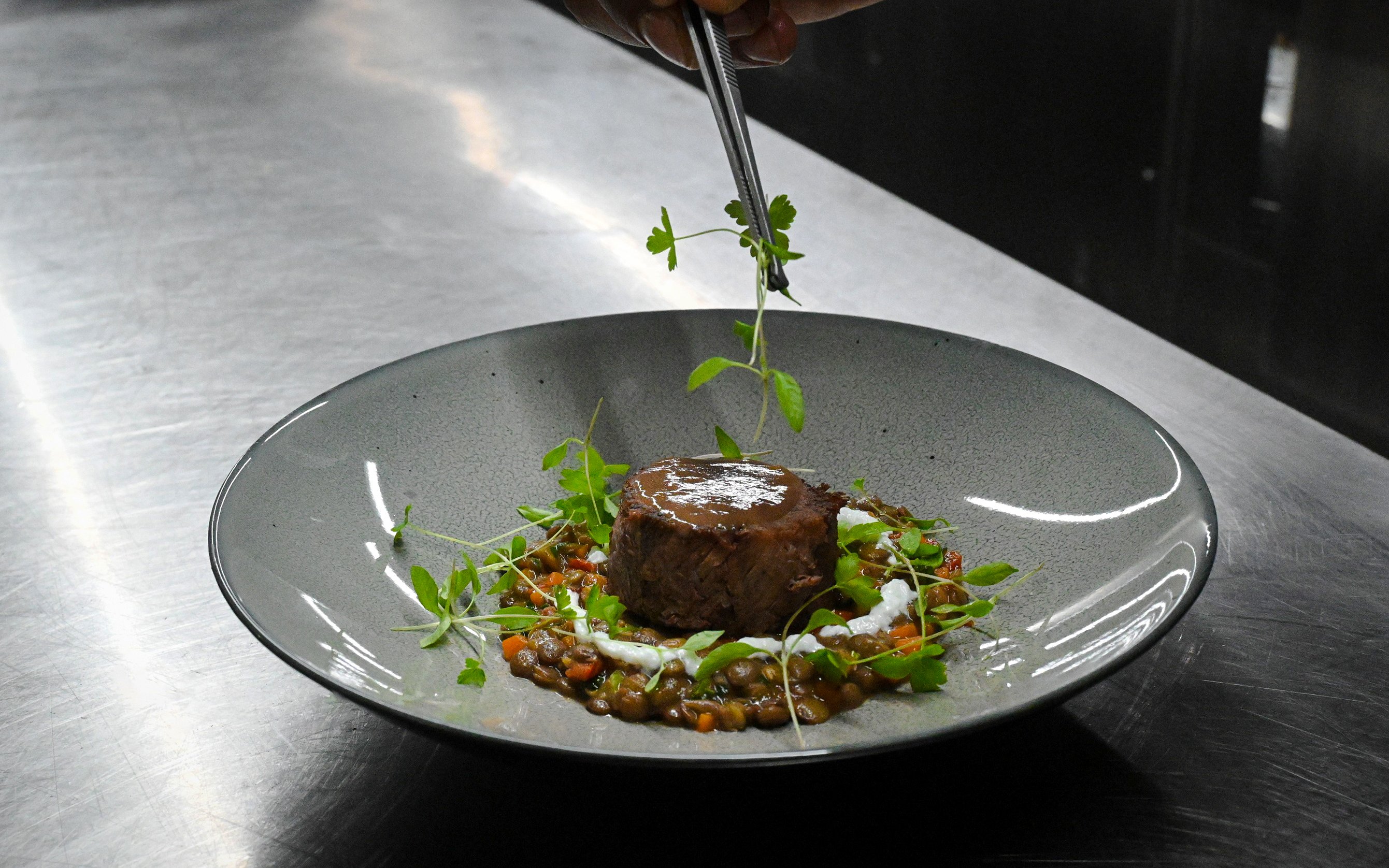Chef plating glazed shin of beef with bone marrow crumb in Bustronome bus, Dubai.
