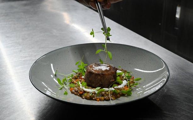 Chef plating glazed shin of beef with bone marrow crumb in Bustronome bus, Dubai.