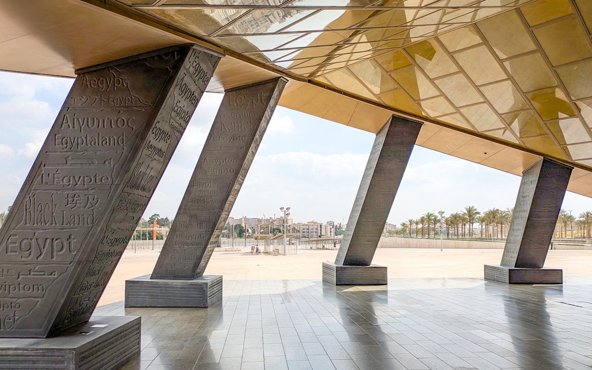 Grand Egyptian Museum entrance with engraved pillars and city view.