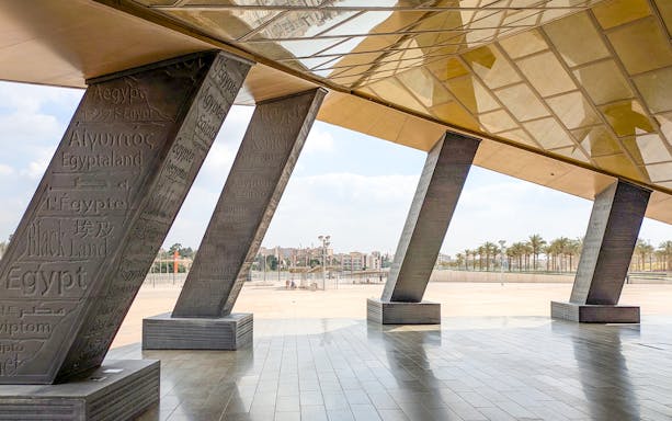 Grand Egyptian Museum entrance with engraved pillars and city view.