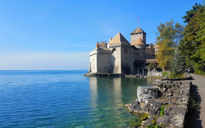 Chillon Castle on Lake Geneva with surrounding trees and clear blue water.