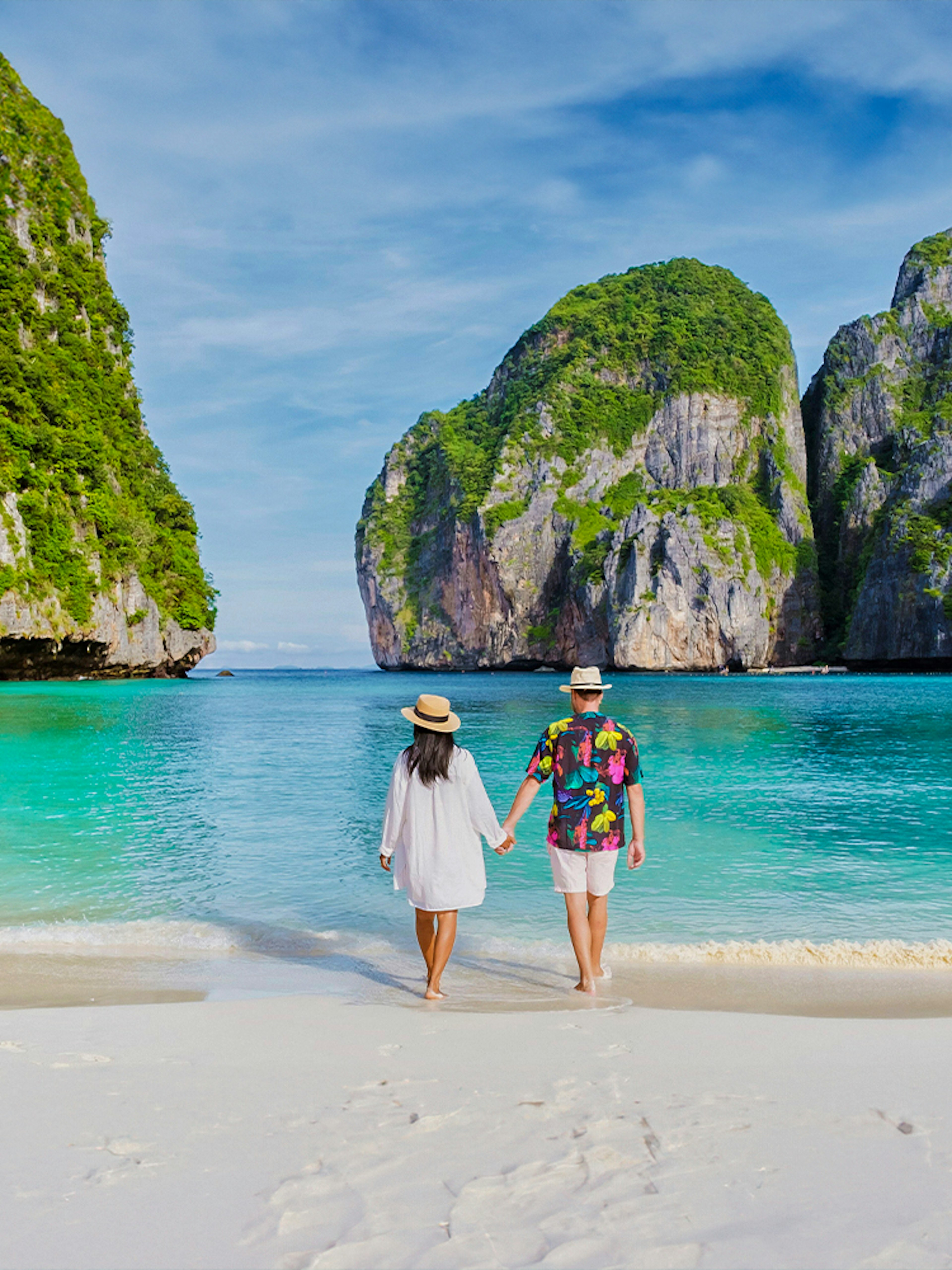 Couple walking on Phi Phi Island beach with limestone cliffs in background.