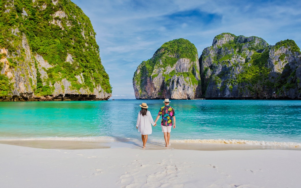 Couple walking on Phi Phi Island beach with limestone cliffs in background.