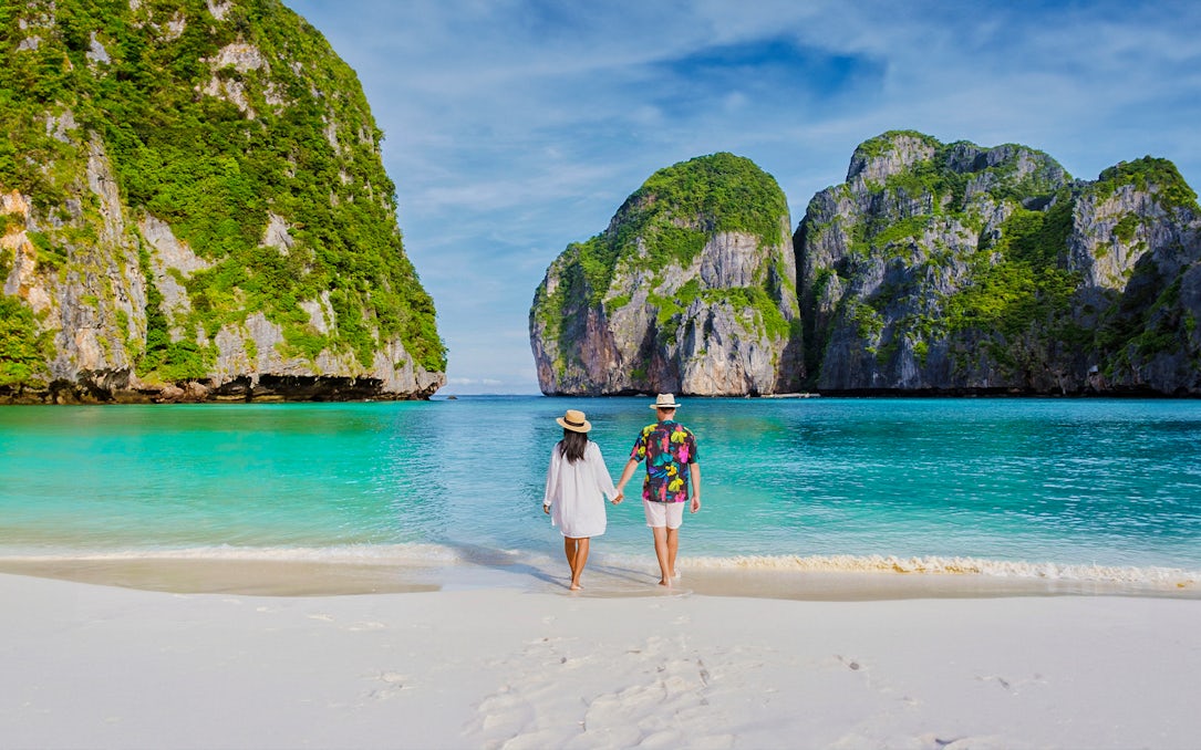 Couple walking on Phi Phi Island beach with limestone cliffs in background.