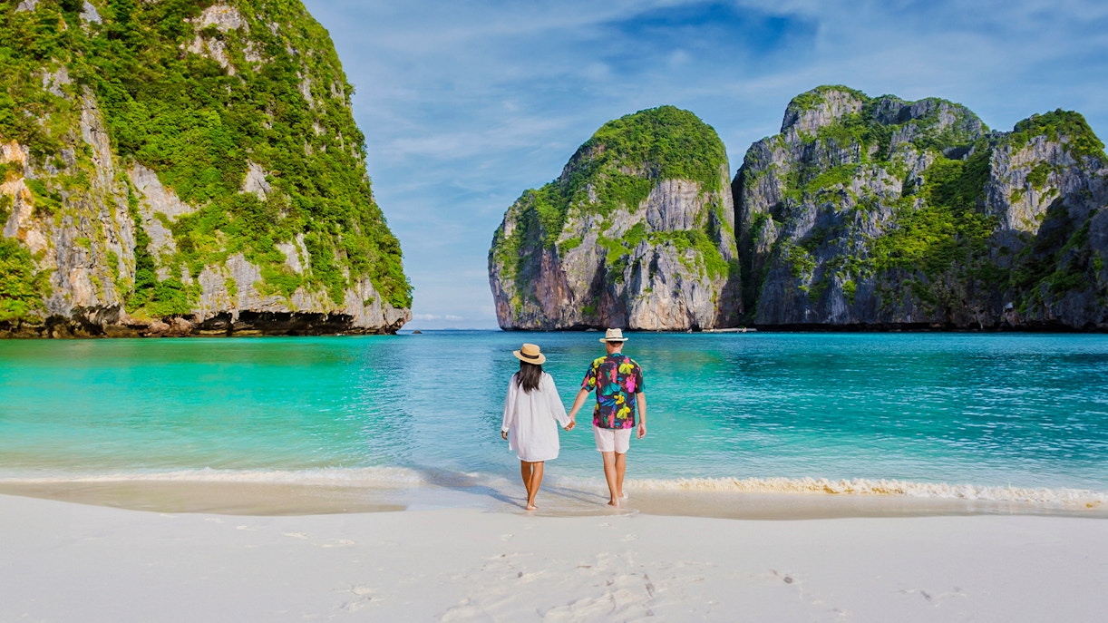 Couple walking on Phi Phi Island beach with limestone cliffs in background.