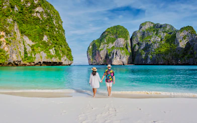 Couple walking on Phi Phi Island beach with limestone cliffs in background.