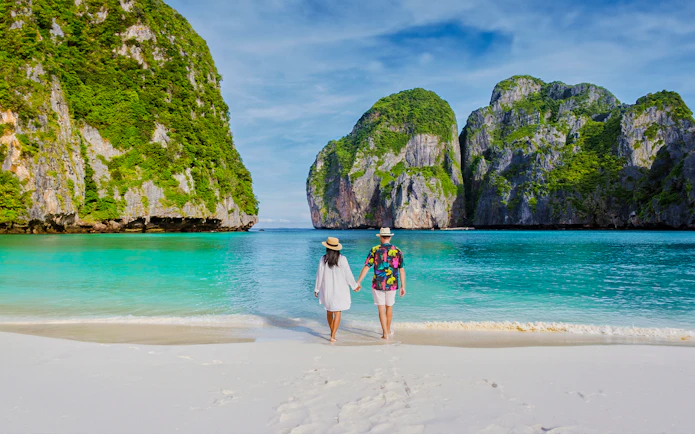 Couple walking on Phi Phi Island beach with limestone cliffs in background.