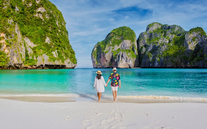 Couple walking on Phi Phi Island beach with limestone cliffs in background.