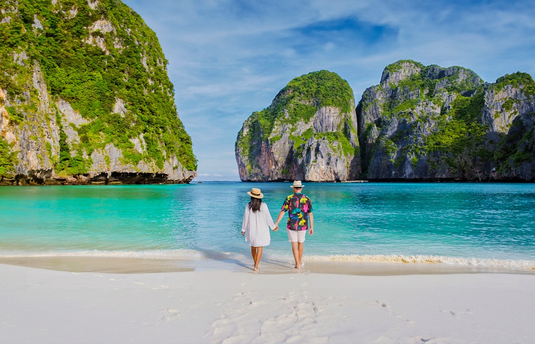 Couple walking on Phi Phi Island beach with limestone cliffs in background.
