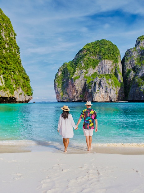 Couple walking on Phi Phi Island beach with limestone cliffs in background.