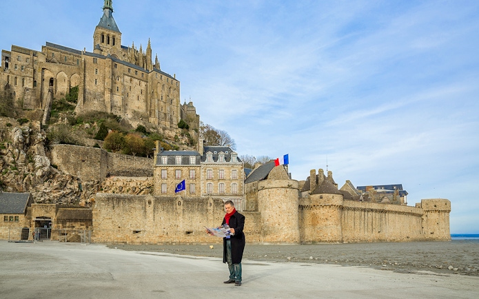 Visitor reading map in front of Mont-Saint-Michel Abbey, France.